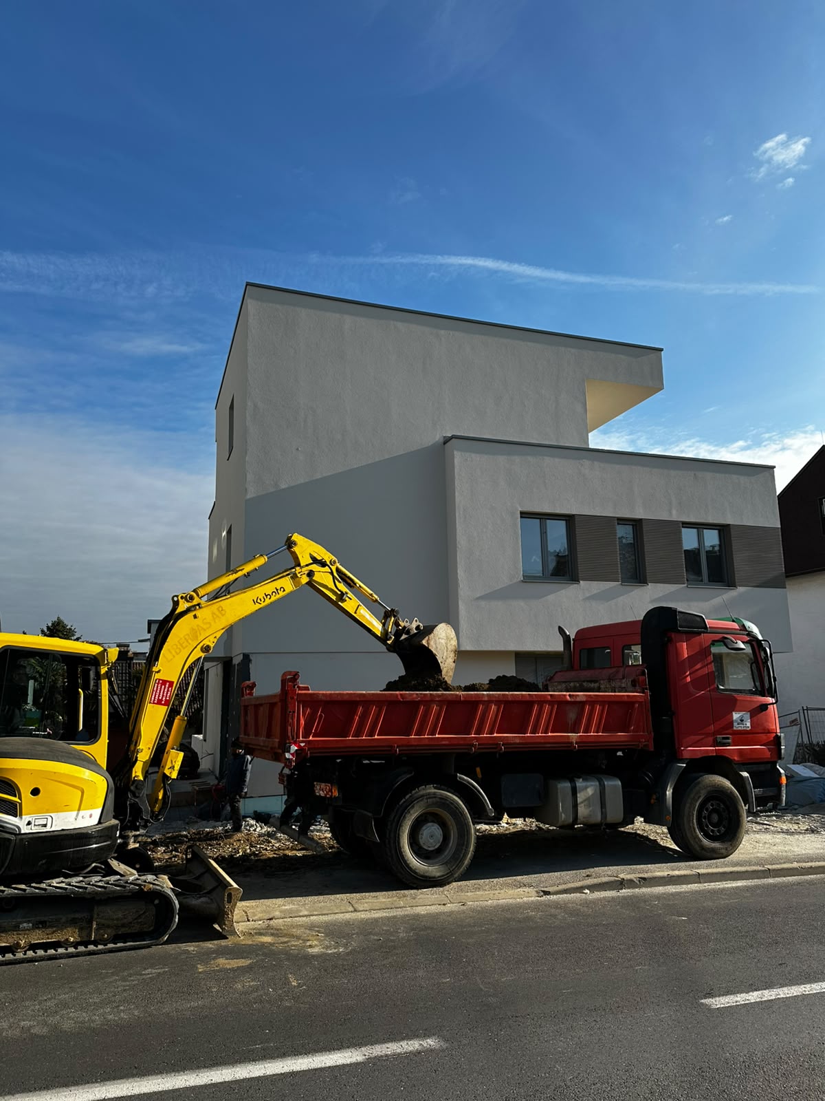 Žuti bager utovaruje materijal u crveni kamion na gradilištu